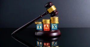 A judge’s gavel beside stacks of coins and blocks spelling “TAX,” symbolizing tax laws, compliance, and financial responsibility.