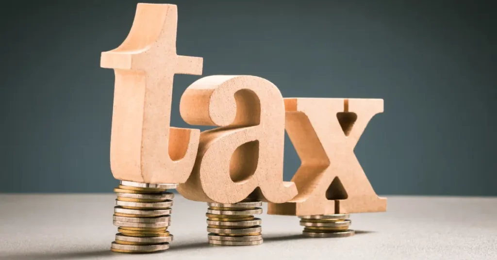 Wooden letters spelling “tax” placed on stacks of coins, representing taxation, financial planning, and money management.