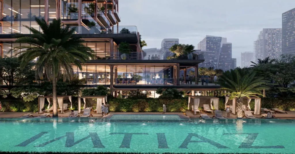 Resort-style swimming pool at The Symphony by Imtiaz, featuring cabanas, palm trees, and the IMTIAZ branding reflected across the turquoise water.