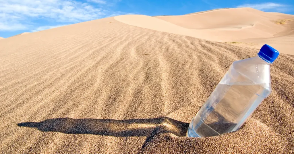 Plastic water bottle half-buried in desert sand representing the UK wealth drain analogy.