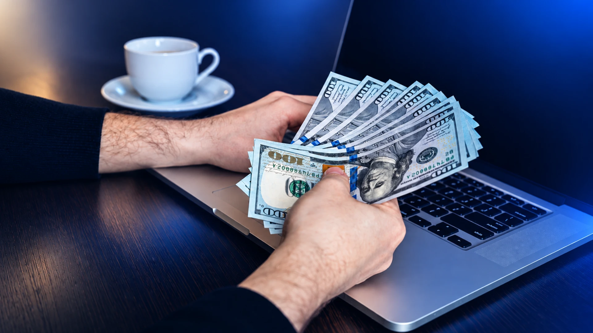 Hands holding U.S. dollar bills over a laptop, representing business banking for non-resident LLC owners.